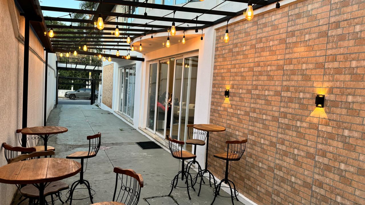 Terraço do Rivê Studio com luzes de filamento e mesas altas de madeira